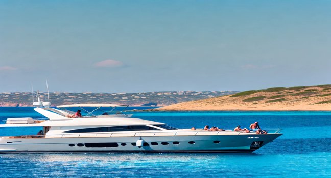 Charter yacht anchored in clear blue waters, with people relaxing on deck and enjoying scenic coastal views