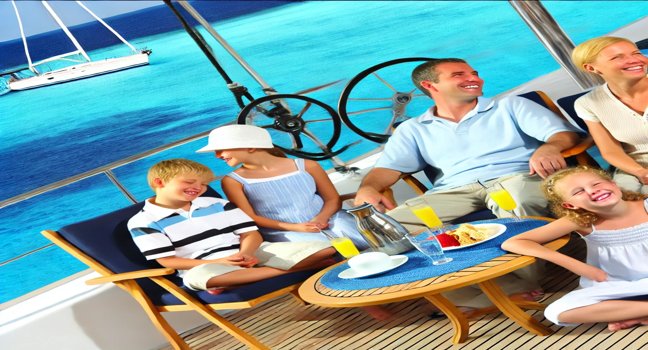 A family enjoying a cruise holiday on a yacht, relaxing and engaging in activities, with clear blue waters and a sunny sky in the background