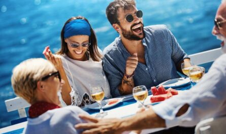 Auf ihrem Kreuzfahrt Urlaub genießt eine fröhliche Gruppe ein gemeinsames Essen an Bord, lacht und entspannt sich auf dem Meer