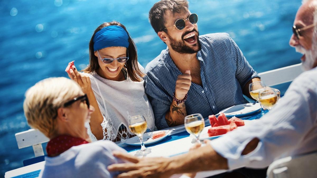 Auf ihrem Kreuzfahrt Urlaub genießt eine fröhliche Gruppe ein gemeinsames Essen an Bord, lacht und entspannt sich auf dem Meer