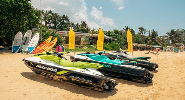 Several colorful jet skis parked on a sandy tropical beach under sunny skies
