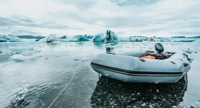 A grey inflatable boat tied near floating icebergs in cold, clear Arctic waters