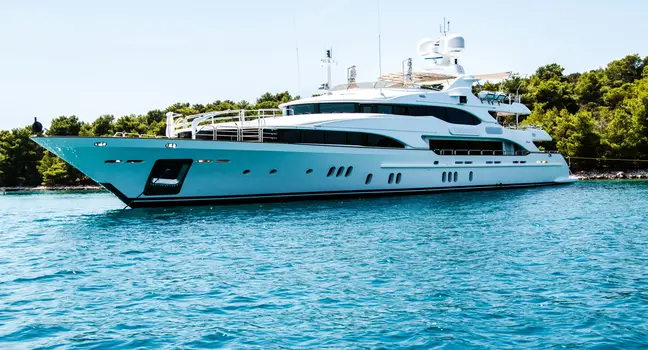 A sleek white luxury yacht anchored on clear blue water near a lush green coastline