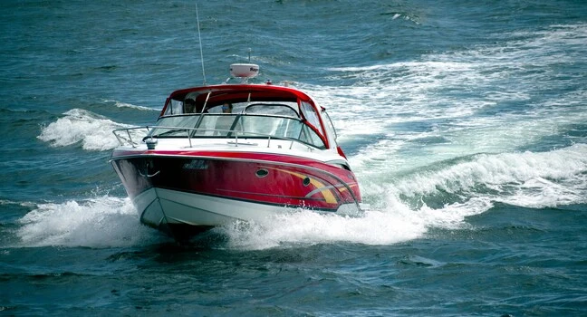 A bright red motorboat speeding across the open blue water, leaving a trail behind