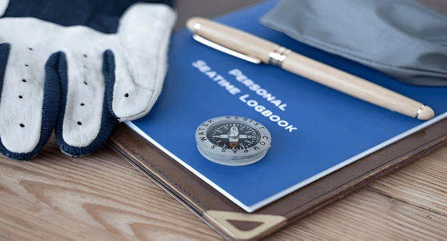 Detailed view of a sailor's logbook about yacht career opportunities, compass and gloves on wooden desk