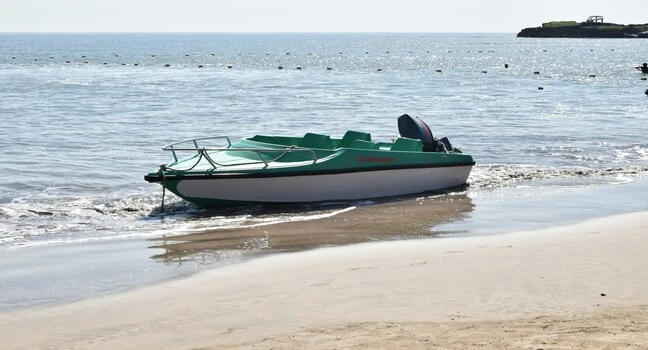A small green motorboat resting on the sandy shore with calm sea in the background