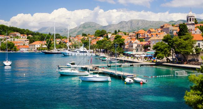 Weiße Segelyacht vor der kroatischen Küste mit Altstadt, Hügeln und blauem Himmel im Hintergrund