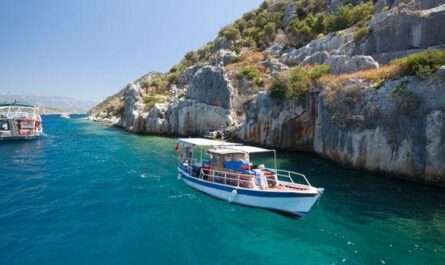 A small tour boat glides through crystal-clear blue waters near rocky coastal cliffs, offering a tranquil and scenic experience