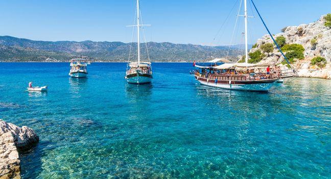 Traditional sailboats rest on turquoise seas with a backdrop of rugged hills and calm skies, capturing the beauty of Mediterranean waters