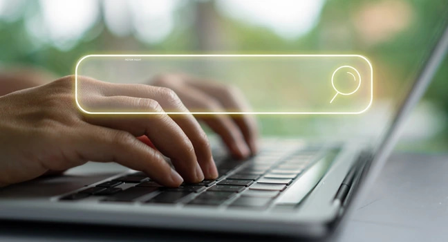 Online-Suche nach der idealen Yacht Hände tippen auf einer Laptop-Tastatur, darüber schwebt ein leuchtendes digitales Suchfeld mit einer Lupe.