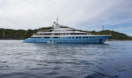 A luxury blue-hulled mega yacht anchored peacefully near a green island