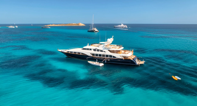 A luxurious charter yacht floating in shallow turquoise waters with other yachts nearby