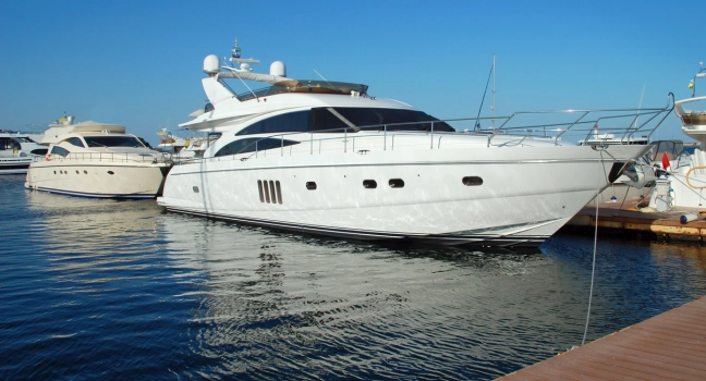 A sleek white motor yacht docked at a marina under clear blue skies