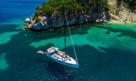 A white sailing yacht anchored in a turquoise cove beside rocky cliffs