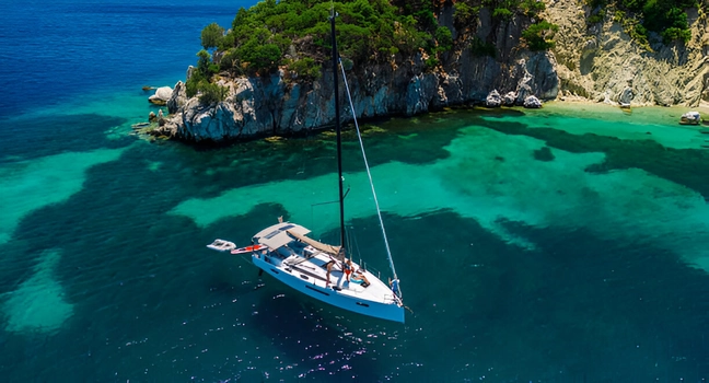 A white sailing yacht anchored in a turquoise cove beside rocky cliffs