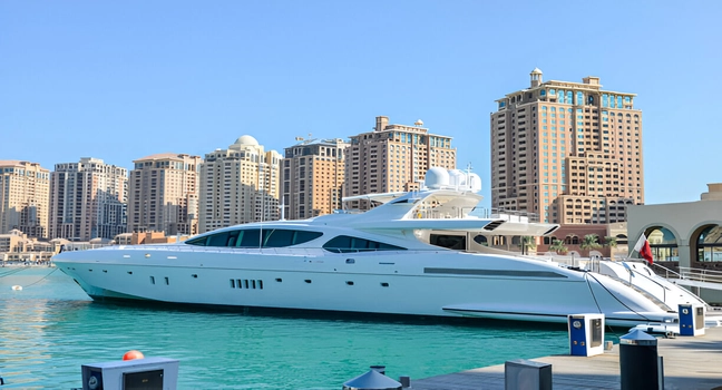 A sleek mega yacht docked in turquoise waters with luxury high-rise buildings behind