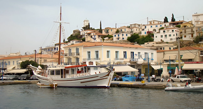 A classic wooden boat docked in a picturesque Greek island harbor with hillside homes Yacht Charter Sicily