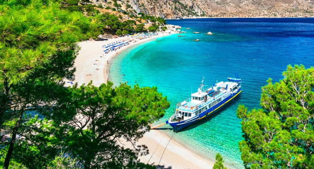Dodekanes Insel Karpathos mit türkisfarbenem Wasser, Boot und geschwungener Strandbucht