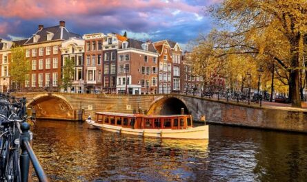 Hausboot auf einer Amsterdamer Gracht mit historischen Häusern im Hintergrund.