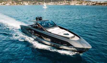 Eine elegante Lamborghini Yacht fährt schnell über das ruhige blaue Meer mit Küstenstadt im Hintergrund