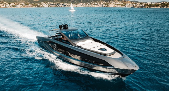 Eine elegante Lamborghini Yacht fährt schnell über das ruhige blaue Meer mit Küstenstadt im Hintergrund