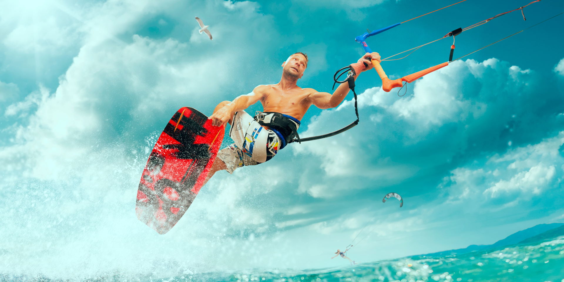 A well-toned athletic man is kitesurfing on a high wave and holding on to the rope