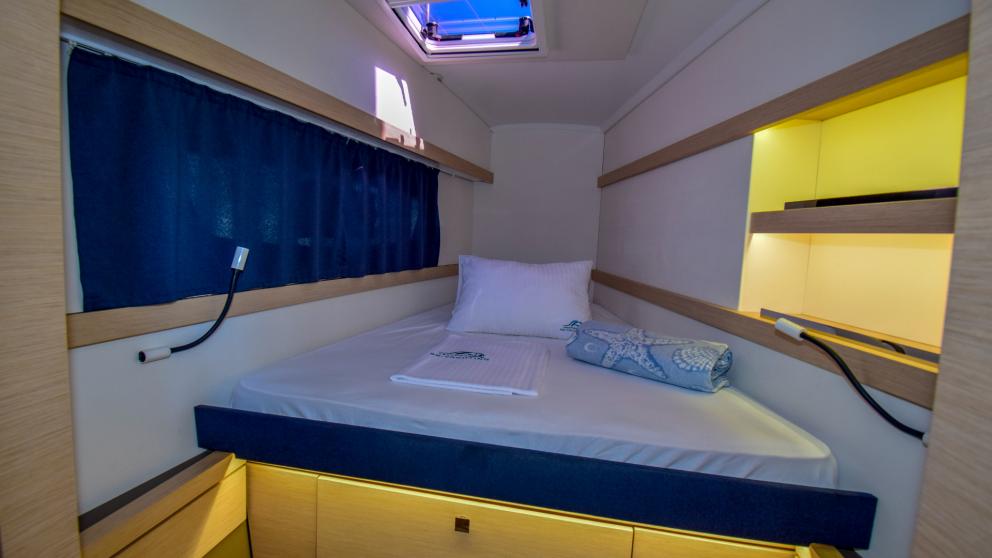 A cabin with a large bed and lighting. You can see the ceiling porthole
