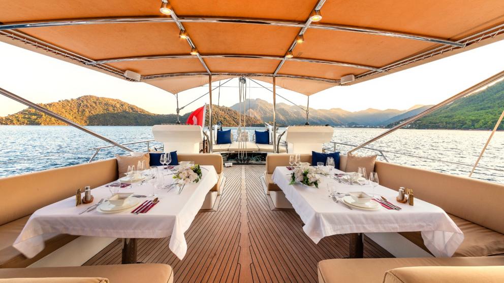 Shaded dining area with set tables on the deck of yacht Ubi Bene at sunset.