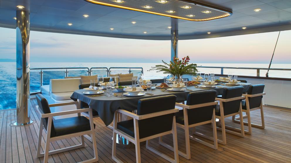 Elegant dining area aboard Anima Maris, set table with sea view at sunset.