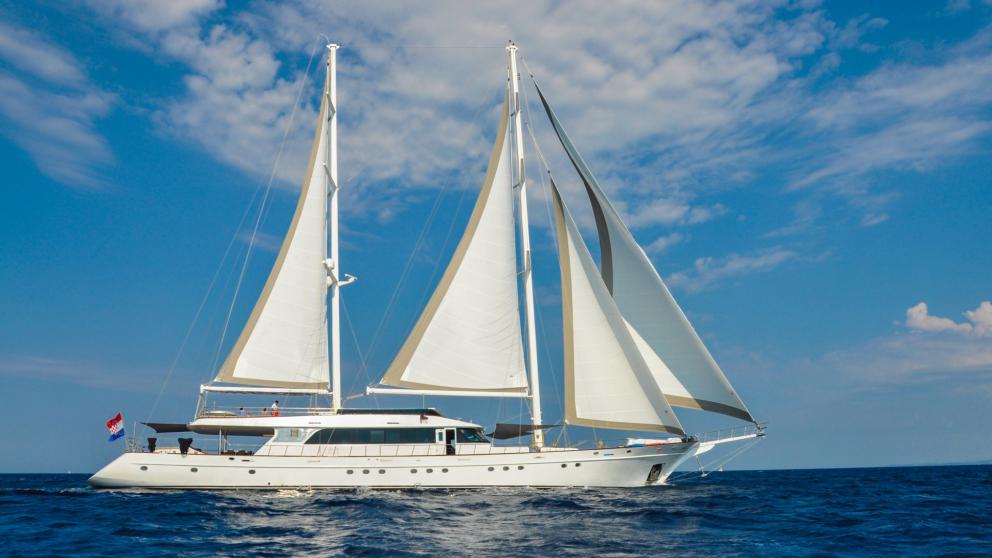 The luxury yacht glides with open sails on the sea under a blue sky.