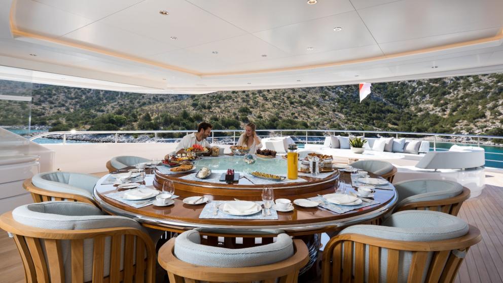 The dining area on the Opari yacht features a round table set with elegant dishes, comfortable chairs, and stunning view