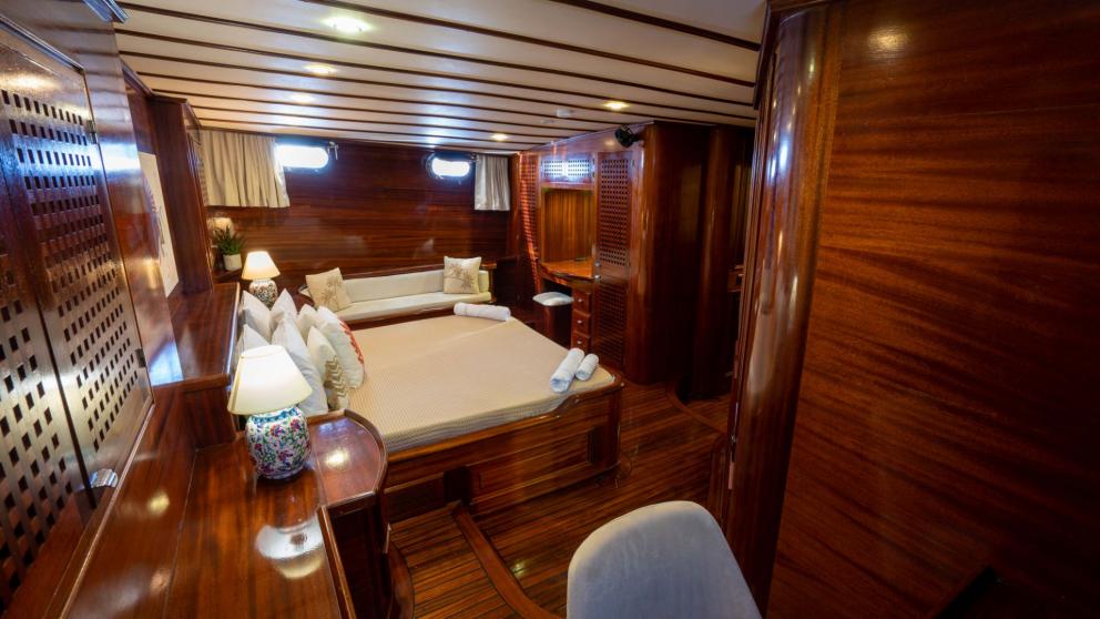 A luxurious cabin on the Gulet Elianora with fine wooden walls, a large bed, a cosy seating area and stylish decoration.