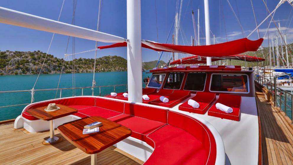 The deck of the Gulet Victoria with red upholstered furniture and a view of the turquoise-coloured water.