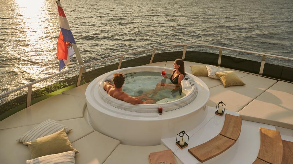 Couple enjoying the hot tub on the deck of Anima Maris with a sea view at sunset.