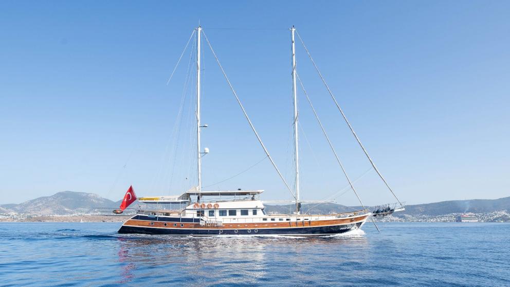 Elegant gulet with two masts and Turkish flag, sailing on calm waters.