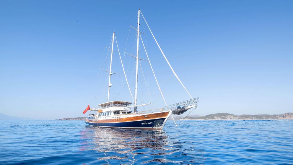 The gulet Oguz Bey anchors on calm, blue waters under a clear sky.