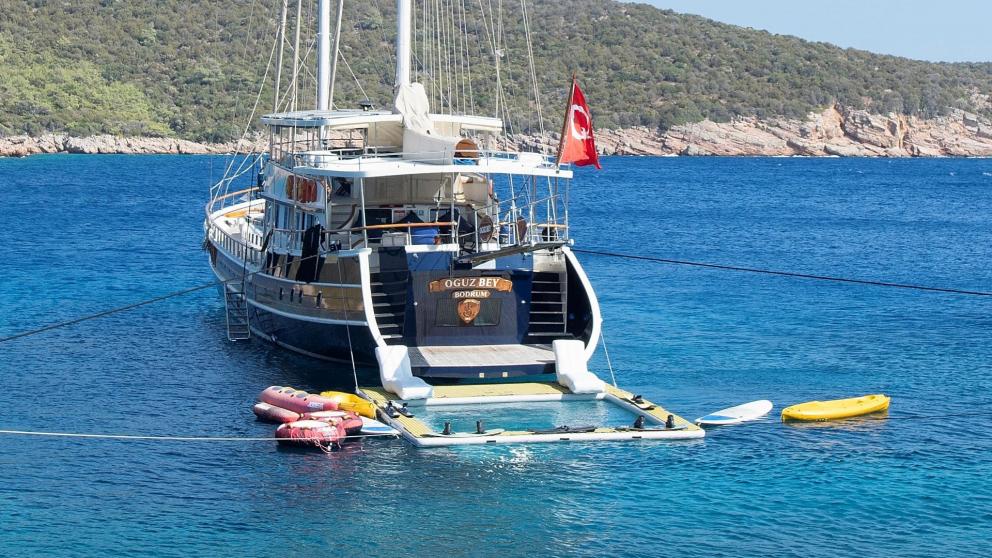 The stern of the gulet Oguz Bey with the Turkish flag, surrounded by turquoise-coloured water and water sports equipment