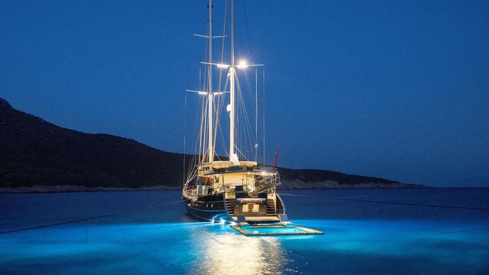 The gulet Oguz Bey at night, illuminated and anchored in the calm, turquoise-coloured water.