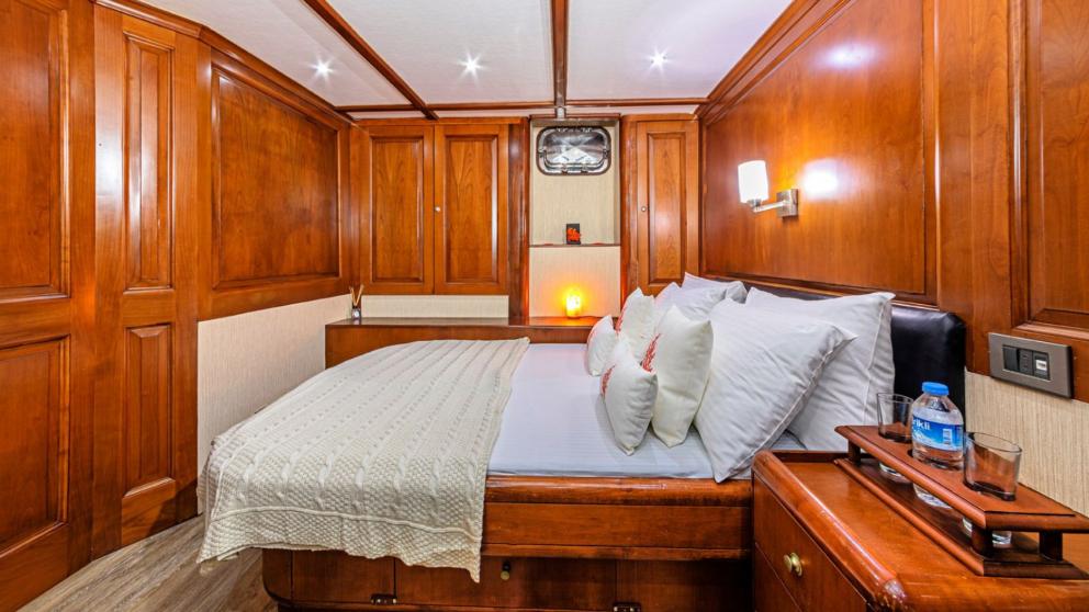 The tidy bedroom of the sailing gulet with white bed linen is decorated for comfortable accommodation.