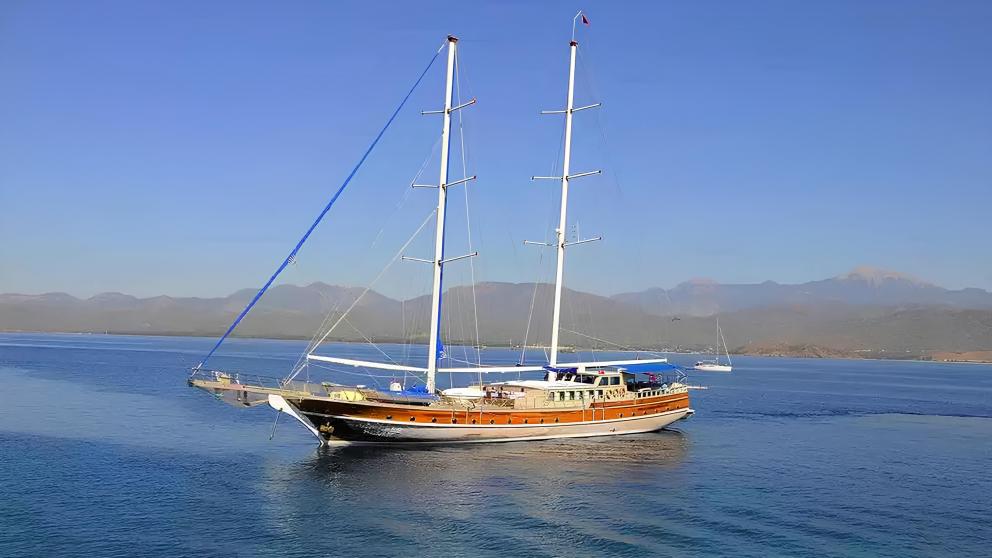 The gulet Prenses Selin, a Turkish wooden sailing boat, lies calmly at sea against a mountain backdrop.