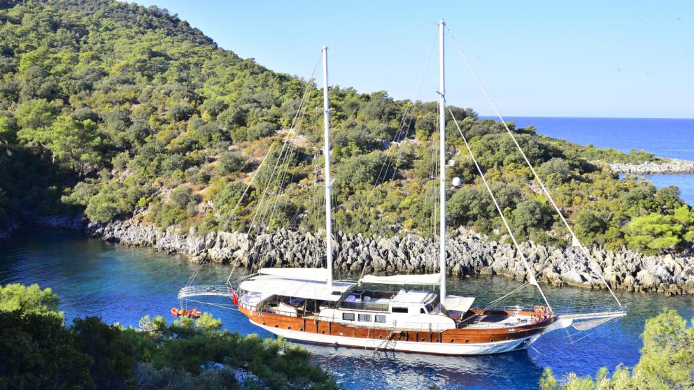 in the two-masted sailing boat Gulet Berrak Su, anchored in a secluded, picturesque bay with green hills.