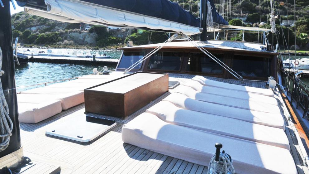 The sun deck of the gulet Elianora in an Italian harbour, equipped with comfortable sun loungers and elegant wood panell