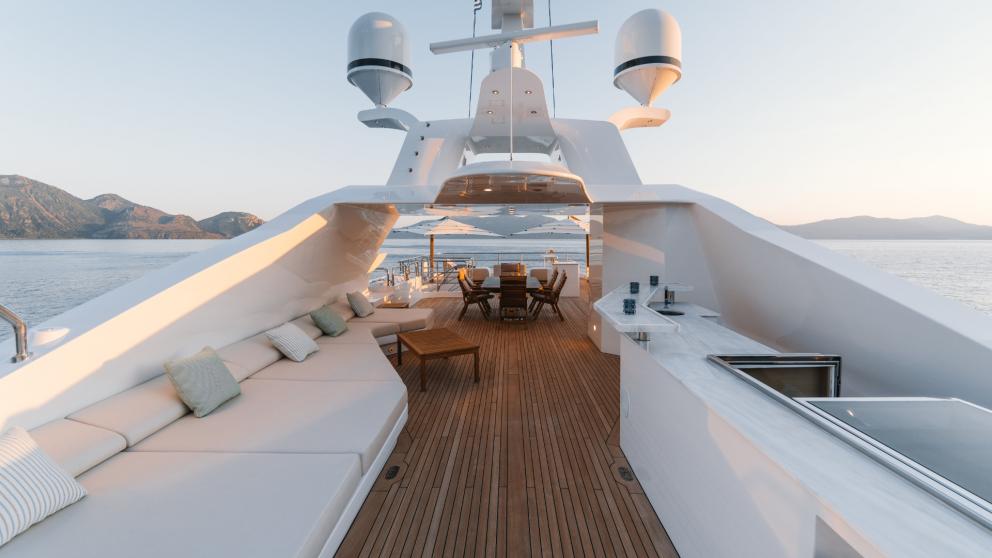 Elegant upper deck of a yacht with comfortable lounges, dining table and marvellous sea views at sunset.