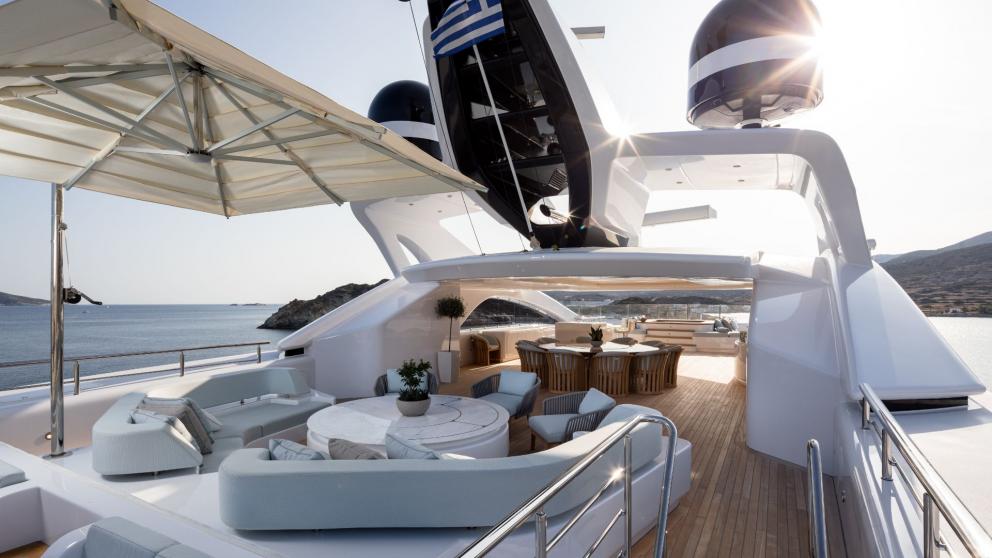 Sun deck on the Opari yacht with comfortable seating, dining area, and views of the sea and coastline.