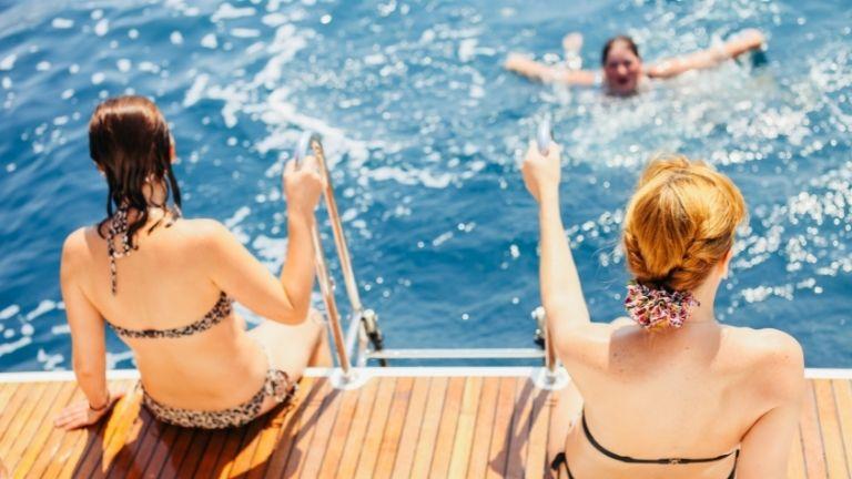 Drei Frauen schwimmen im Meer, indem sie in ihren Bikinis vom Boot springen.