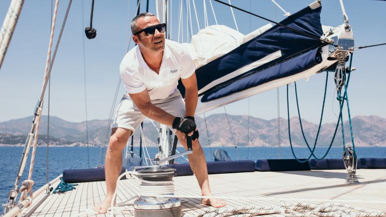 A man in a white T-shirt and shorts hoists the sails