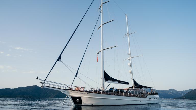 S/Y Voyage luxury gulet at sea with sails down, surrounded by majestic mountains
