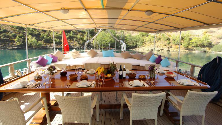 A luxuriously laid dining table on the deck of the gulet Prenses Selin, surrounded by green hills.