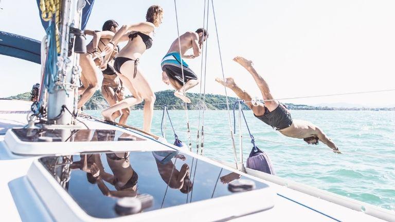 Crowd and group of young people having fun jumping into the sea together.