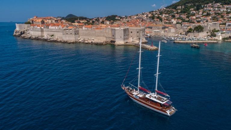 A luxurious 5-cabin Gulet, Adriatic Holiday, sailing near Dubrovnik's historic city walls under a clear blue sky.